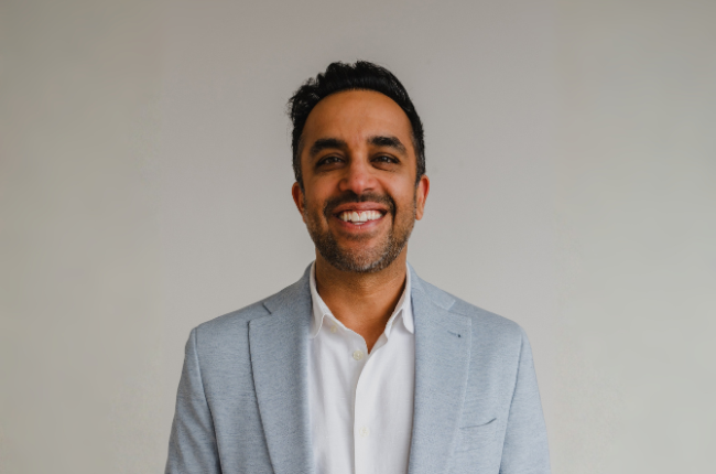 Neil Pasricha, smiling portrait in a light gray blazer and white shirt against a neutral background.