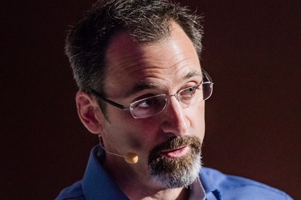 Maurice Conti, portrait with glasses, a goatee, and a headset microphone while speaking.
