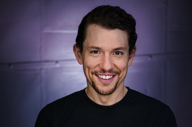 Miguel Cervantes, Smiling Portrait With A Goatee And Black Shirt Against A Purple Background.