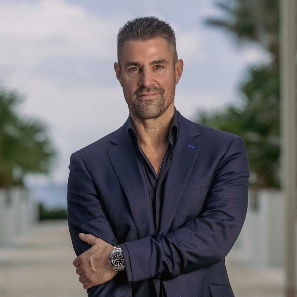 Professional portrait of Kevin Boehm standing outdoors with arms crossed in a navy suit.