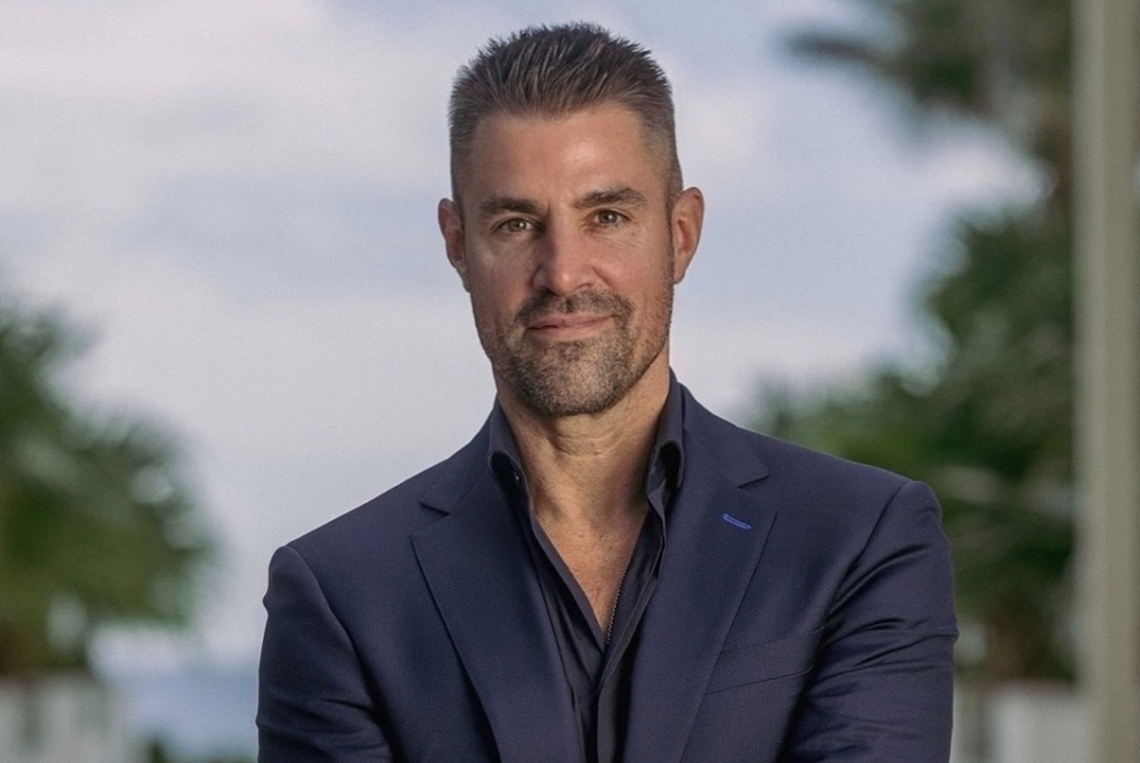 Professional portrait of Kevin Boehm standing outdoors with arms crossed in a navy suit.