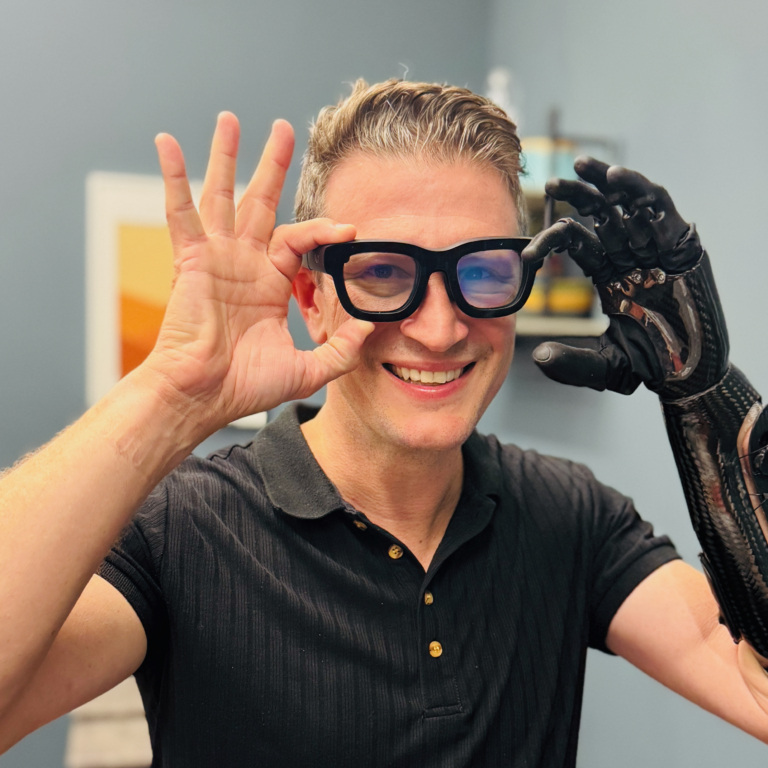 Loyal Pyczynski, Smiling Portrait Wearing Glasses And A Black Prosthetic Arm.