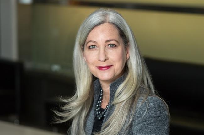 marci rossell smiling, wearing grey jacket and pearl necklace